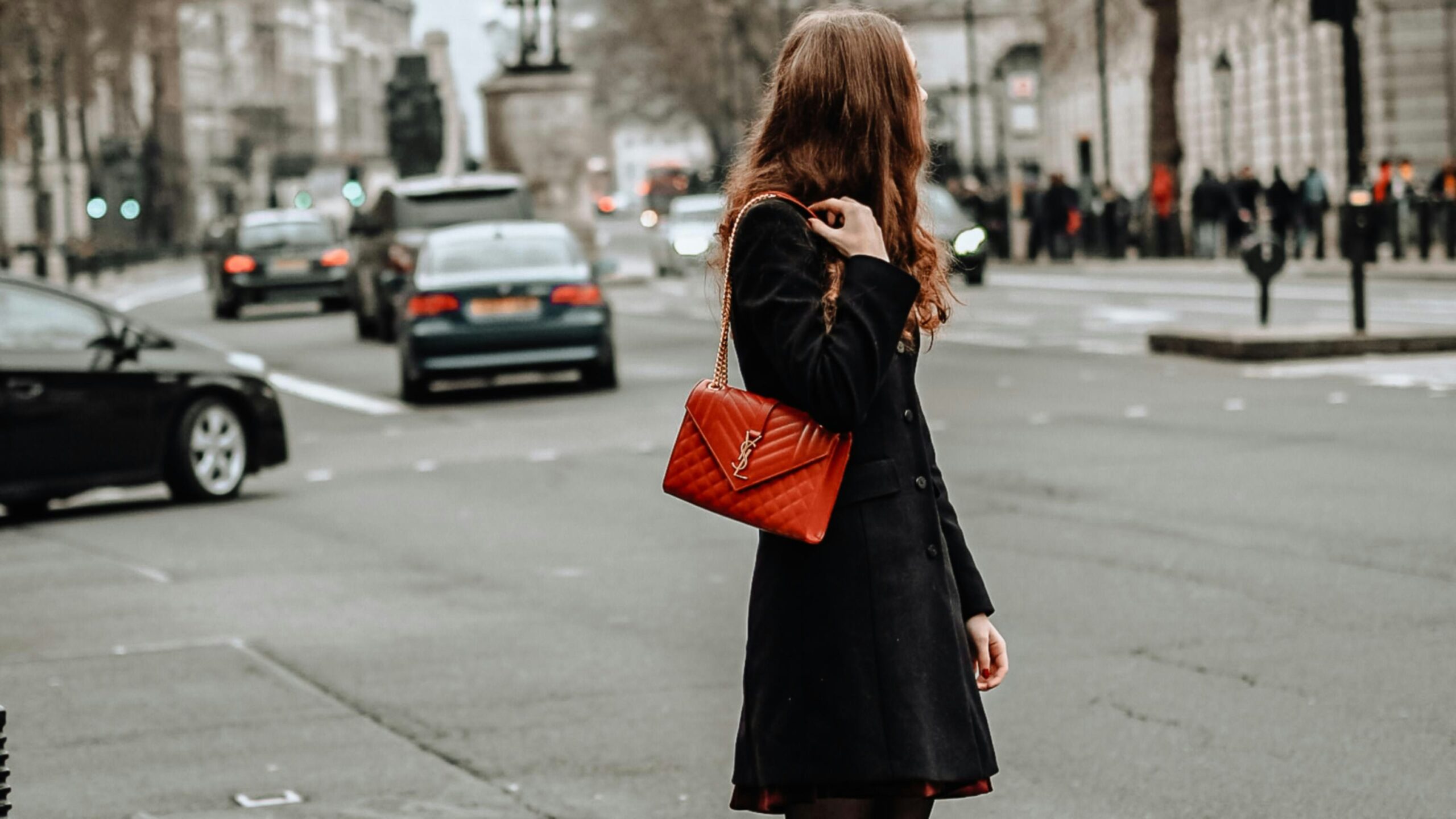 Fille traversant la route avec un sac à main de luxe rouge, ajoutant une touche d'élégance à son look urbain