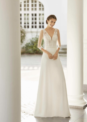 Robe de mariée Adriana Alier modèle Salder avec coupe droite, manches mi-longues en dentelle, et encolure en V, portée par une mariée dans un décor lumineux et romantique