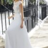 eune femme souriante portant une robe de mariée blanche élégante avec un haut en dentelle florale complexe, montant des marches en extérieur près de clôtures en fer forgé