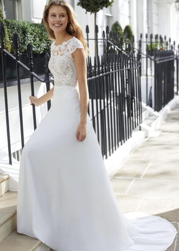 eune femme souriante portant une robe de mariée blanche élégante avec un haut en dentelle florale complexe, montant des marches en extérieur près de clôtures en fer forgé