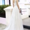 Vue arrière d'une élégante robe de mariée en dentelle avec une jupe fluide, une ouverture en V délicate dans le dos et un cadre urbain coloré de maisons pastel
