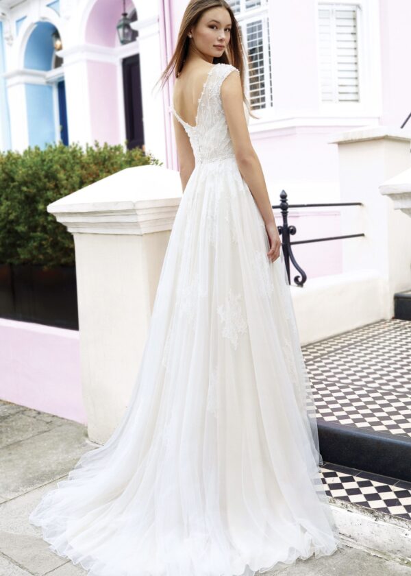 Vue arrière d'une élégante robe de mariée en dentelle avec une jupe fluide, une ouverture en V délicate dans le dos et un cadre urbain coloré de maisons pastel
