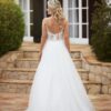 Vue arrière d'une robe de mariée en tulle avec un dos nu décoré de dentelle délicate, posant devant une villa aux marches en pierre.