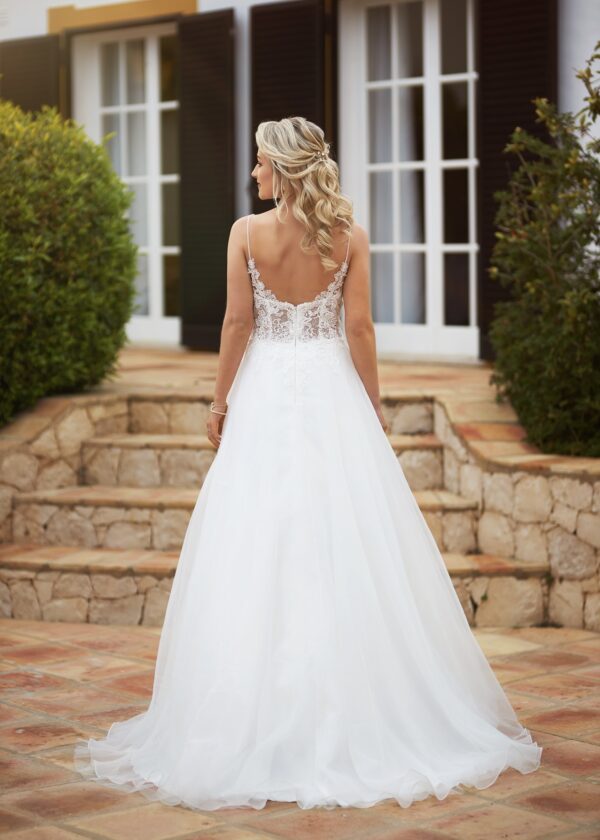Vue arrière d'une robe de mariée en tulle avec un dos nu décoré de dentelle délicate, posant devant une villa aux marches en pierre.