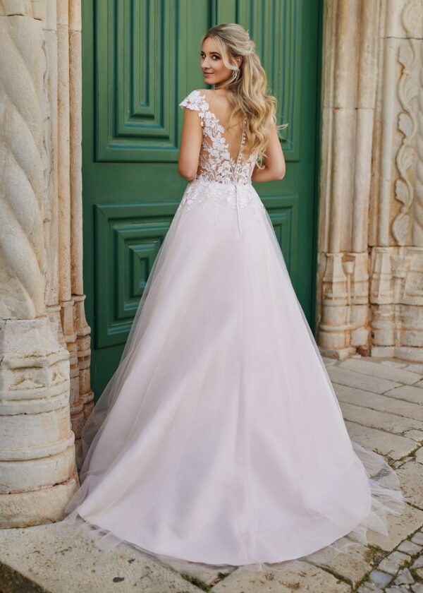 Robe de mariée dos en dentelle florale avec jupe fluide à traîne, présentée dans un cadre architectural rustique et romantique