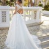 Une mariée en robe blanche avec un corsage en dentelle et un marié en costume bleu agenouillé, tenant une bague dans un jardin romantique.