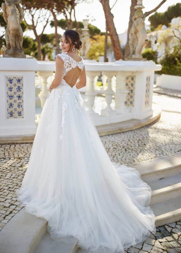 Une mariée en robe blanche avec un corsage en dentelle et un marié en costume bleu agenouillé, tenant une bague dans un jardin romantique.