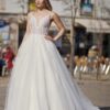 Mariée en robe blanche à décolleté en V profond, corsage en dentelle, jupe volumineuse fluide ornée de détails scintillants, posant dans une place urbaine sous un ciel ensoleillé