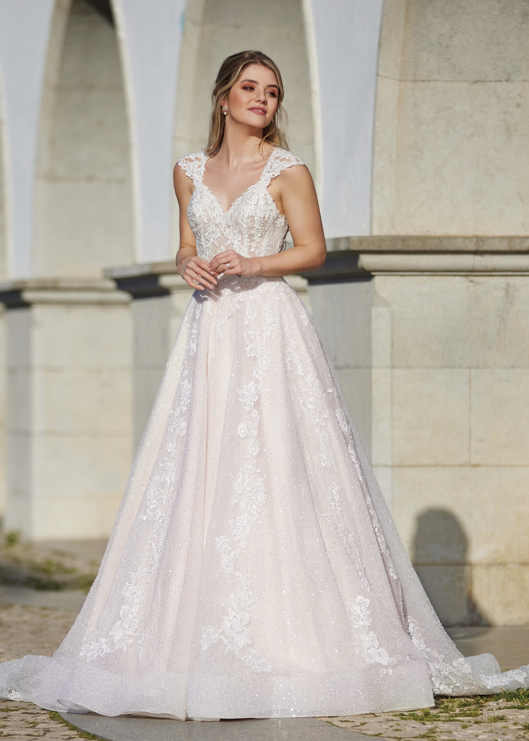 Robe de mariée élégante avec dentelle délicate et décolleté plongeant, prise en photo devant des arches en pierre