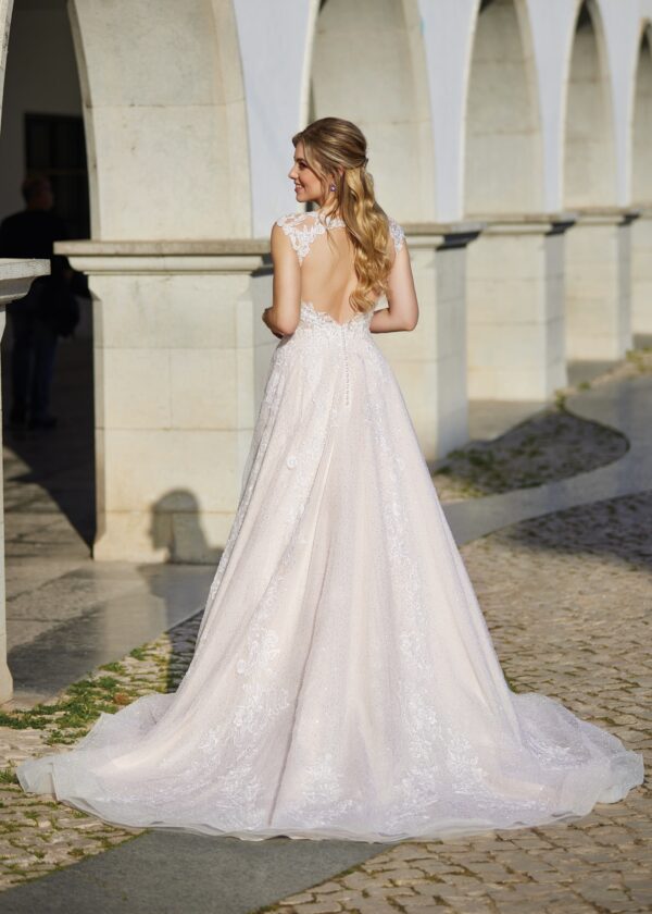Vue arrière d'une robe de mariée avec un dos ouvert et une jupe en dentelle scintillante, devant des arches historiques en pierre