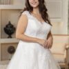 Portrait en plan rapproché d'une mariée souriante portant une robe blanche avec des détails en dentelle sur le corsage et les manches. En arrière-plan, un décor chaleureux avec des étagères et des éléments de décoration élégants