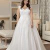 Mariée debout dans une robe de mariée blanche avec des détails en dentelle et une jupe volumineuse. Elle se tient dans un salon élégant, entourée de meubles raffinés et d'une décoration chaleureuse