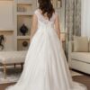 Vue de dos d'une mariée dans une robe de mariée blanche avec une traîne élégante, un dos en dentelle délicate et des détails boutonnés, posant dans un salon sophistiqué et chaleureux