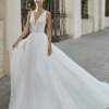 Mariée dans une élégante robe de mariée blanche à décolleté plongeant, brodée de dentelle, avec une jupe en tulle fluide et légère, posant devant un portail orné