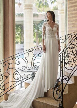 Mariée élégante portant une robe de mariée avec un haut en dentelle à manches longues et une jupe fluide, posant sur un escalier orné de fer forgé