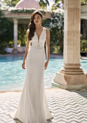 Mariée élégante portant une robe de mariée ajustée avec un décolleté en V profond et des détails scintillants à la taille, posant devant une piscine
