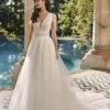 Mariée posant élégamment en robe de mariée avec un décolleté en V profond près d'une piscine, dans un cadre romantique en extérieur