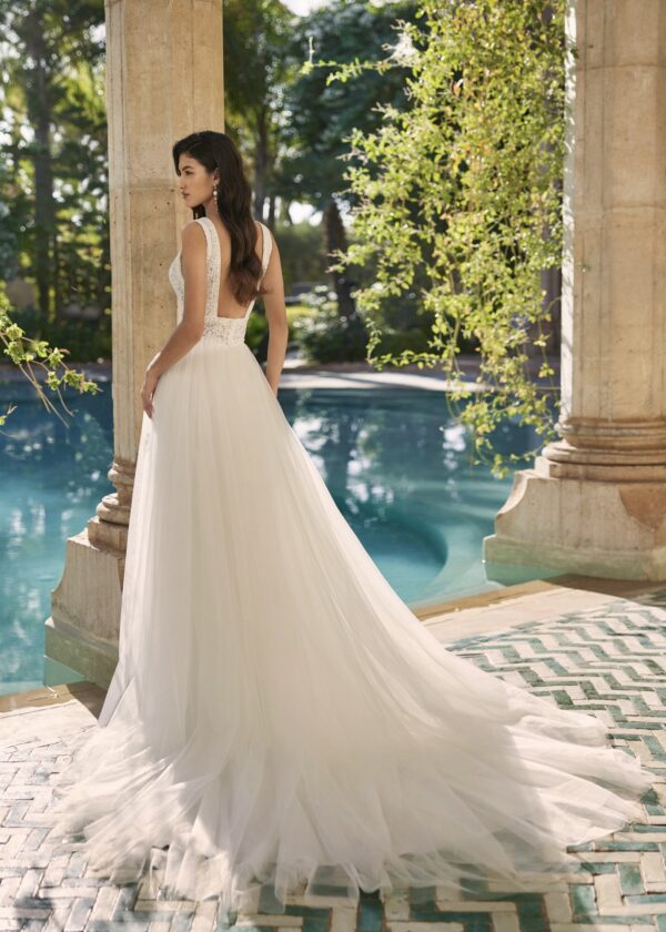 Mariée de dos en robe de mariée avec dos plongeant, posant près d'une piscine dans un cadre romantique en plein air