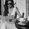 Mariée élégante portant des lunettes de soleil, lisant un journal tout en prenant un petit-déjeuner, photographie en noir et blanc