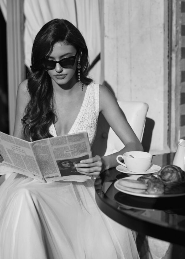 Mariée élégante portant des lunettes de soleil, lisant un journal tout en prenant un petit-déjeuner, photographie en noir et blanc