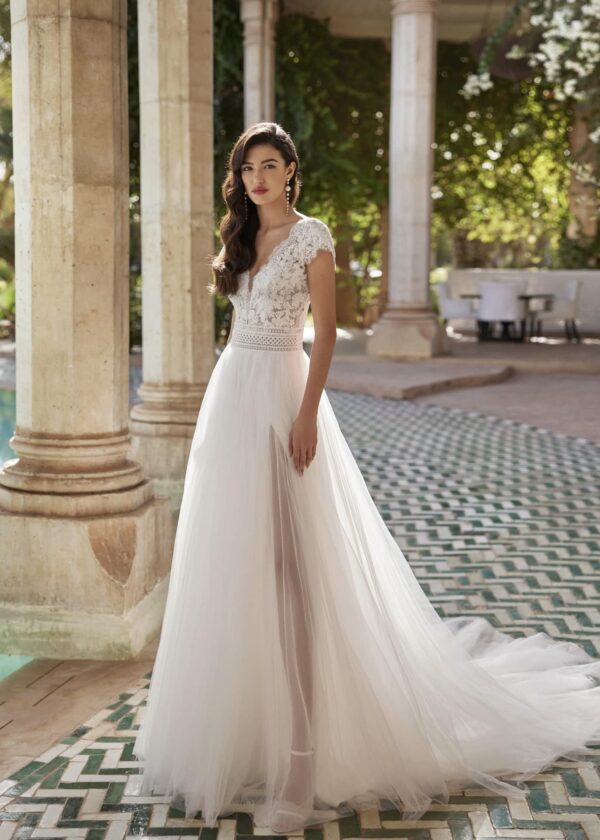 Mariée en robe de mariée avec corsage en dentelle et fente latérale, posant devant des colonnes en pierre