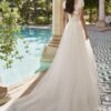 Mariée de dos avec une robe en dentelle et traîne en tulle, posant près d'une piscine dans un cadre extérieur romantique