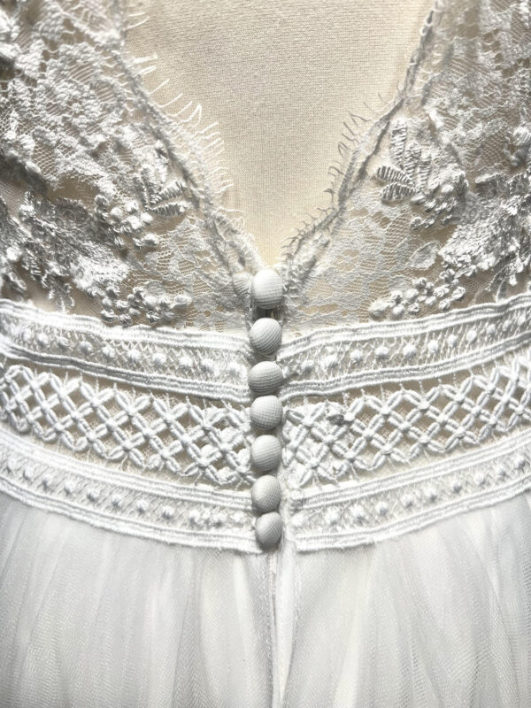 Mariée en robe de mariée avec corsage en dentelle et fente latérale, posant devant des colonnes en pierre