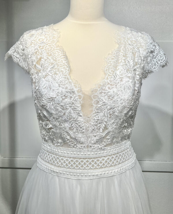 Mariée en robe de mariée avec corsage en dentelle et fente latérale, posant devant des colonnes en pierre