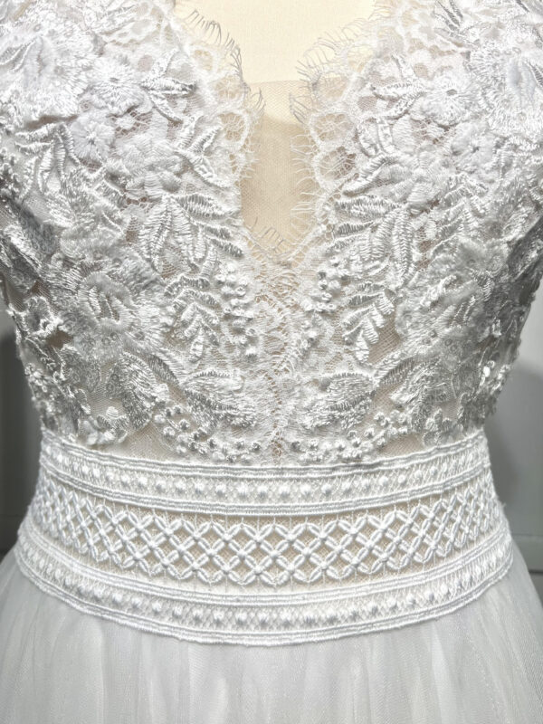 Mariée en robe de mariée avec corsage en dentelle et fente latérale, posant devant des colonnes en pierre