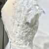 Mariée en robe de mariée avec corsage en dentelle et fente latérale, posant devant des colonnes en pierre