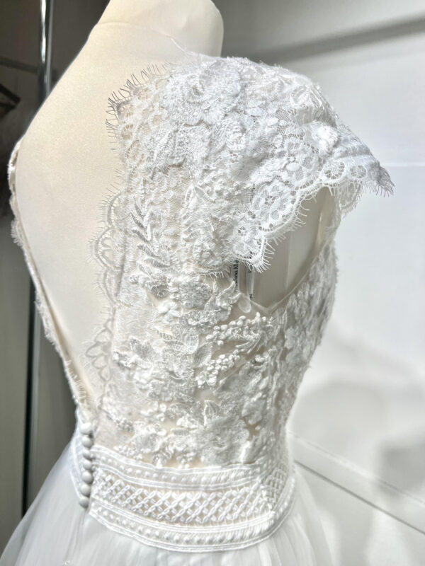Mariée en robe de mariée avec corsage en dentelle et fente latérale, posant devant des colonnes en pierre