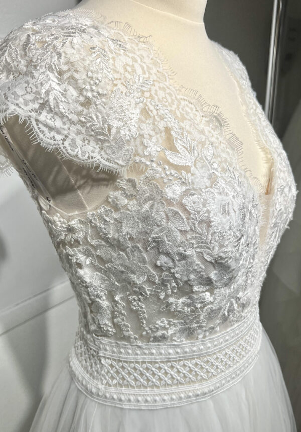Mariée en robe de mariée avec corsage en dentelle et fente latérale, posant devant des colonnes en pierre
