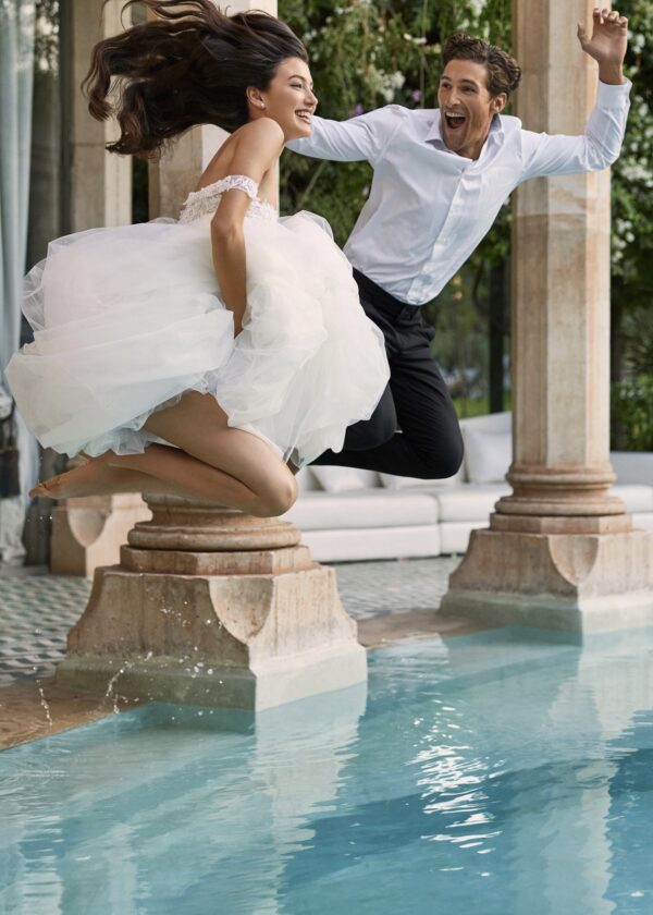 Mariée et marié sautant ensemble dans une piscine, sourire aux lèvres, dans un cadre de mariage amusant et décontracté