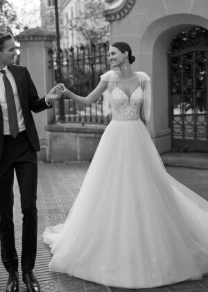 Mariée en robe de mariée romantique avec épaules dénudées et rubans, marchant avec son partenaire dans un cadre urbain en noir et blanc
