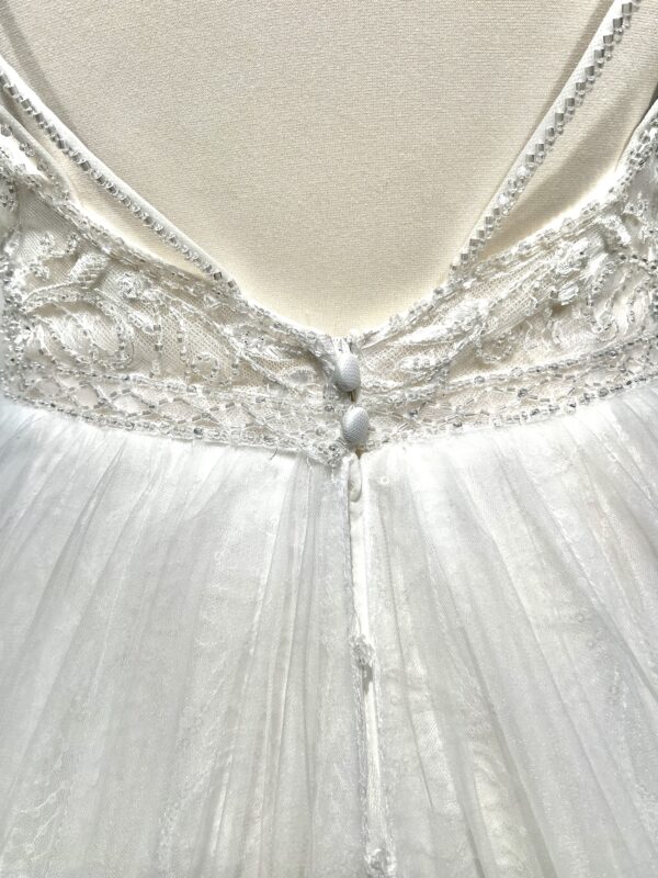 Robe de mariée princesse en tulle pailleté, avec un décolleté en V profond, un bustier orné de pierreries, un dos nu sublimé par des bretelles délicates et des nœuds en tulle aux épaules.