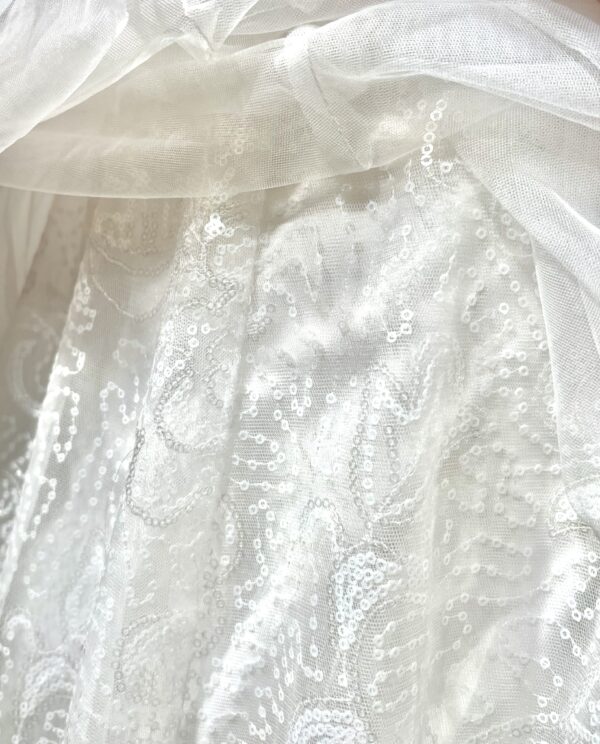 Robe de mariée princesse en tulle pailleté, avec un décolleté en V profond, un bustier orné de pierreries, un dos nu sublimé par des bretelles délicates et des nœuds en tulle aux épaules.