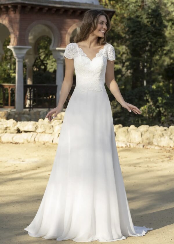Robe de mariée élégante et romantique, dotée d'un corsage en dentelle florale finement travaillée, avec des manches courtes festonnées et une jupe fluide en mousseline légère, idéale pour un mariage en extérieur ou un cadre champêtre