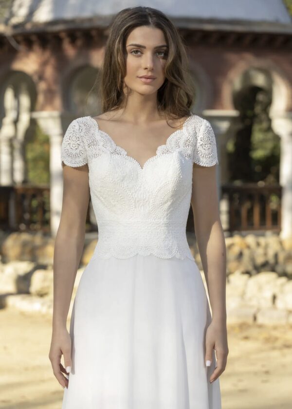 Robe de mariée élégante avec un corsage en dentelle délicatement festonné, des manches courtes raffinées et une jupe en tissu fluide, idéale pour un mariage romantique en extérieur.