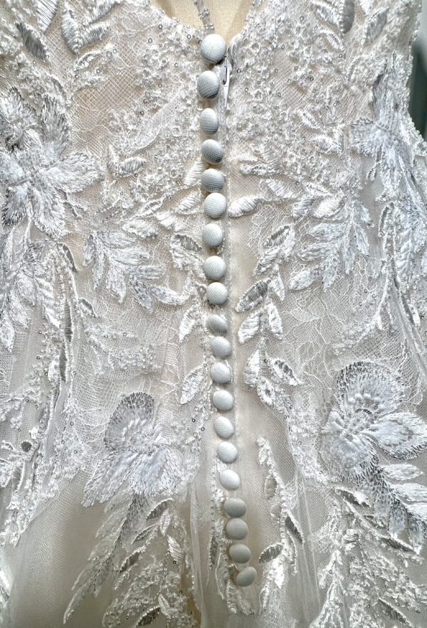 Mariée portant une robe de mariée en tulle avec un décolleté en cœur, broderies florales et bretelles fines, posant dans un jardin ensoleillé