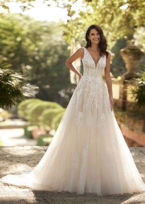Mariée portant une robe de mariée en tulle avec un décolleté en cœur, broderies florales et bretelles fines, posant dans un jardin ensoleillé