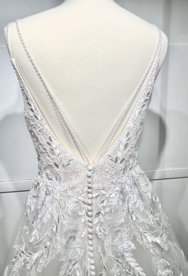 Mariée portant une robe de mariée en tulle avec un décolleté en cœur, broderies florales et bretelles fines, posant dans un jardin ensoleillé
