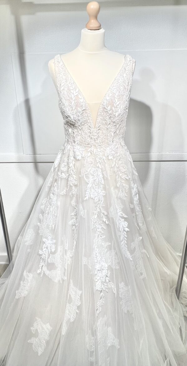 Mariée portant une robe de mariée en tulle avec un décolleté en cœur, broderies florales et bretelles fines, posant dans un jardin ensoleillé
