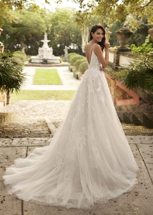 Vue arrière d'une mariée portant une robe de mariée en tulle avec un dos en V et une traîne fluide, dans un jardin fleuri