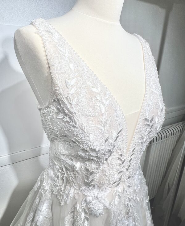 Mariée portant une robe de mariée en tulle avec un décolleté en cœur, broderies florales et bretelles fines, posant dans un jardin ensoleillé