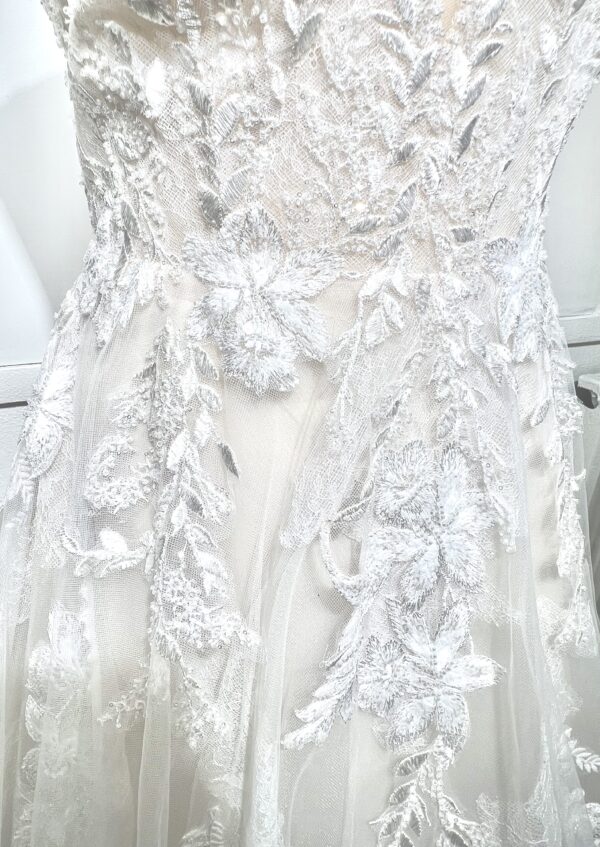 Mariée portant une robe de mariée en tulle avec un décolleté en cœur, broderies florales et bretelles fines, posant dans un jardin ensoleillé