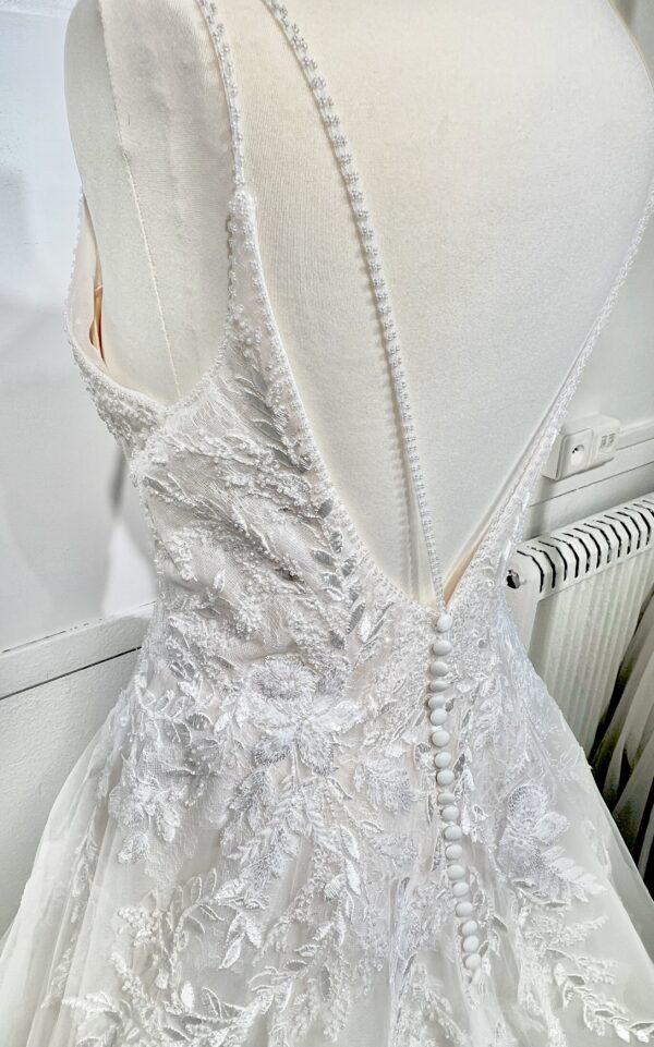 Mariée portant une robe de mariée en tulle avec un décolleté en cœur, broderies florales et bretelles fines, posant dans un jardin ensoleillé