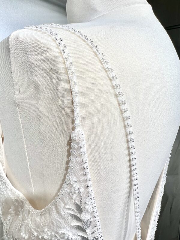 Mariée portant une robe de mariée en tulle avec un décolleté en cœur, broderies florales et bretelles fines, posant dans un jardin ensoleillé