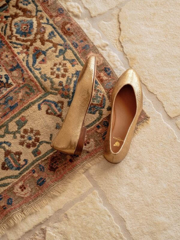 Sandales dorées à lanières fines posées sur un sol en pierre naturelle, offrant une vue complète de leur silhouette moderne.