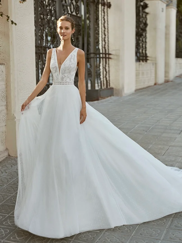 Mariée dans une élégante robe de mariée blanche à décolleté plongeant, brodée de dentelle, avec une jupe en tulle fluide et légère, posant devant un portail orné