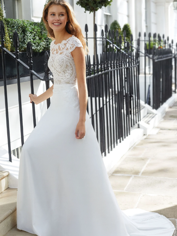 eune femme souriante portant une robe de mariée blanche élégante avec un haut en dentelle florale complexe, montant des marches en extérieur près de clôtures en fer forgé